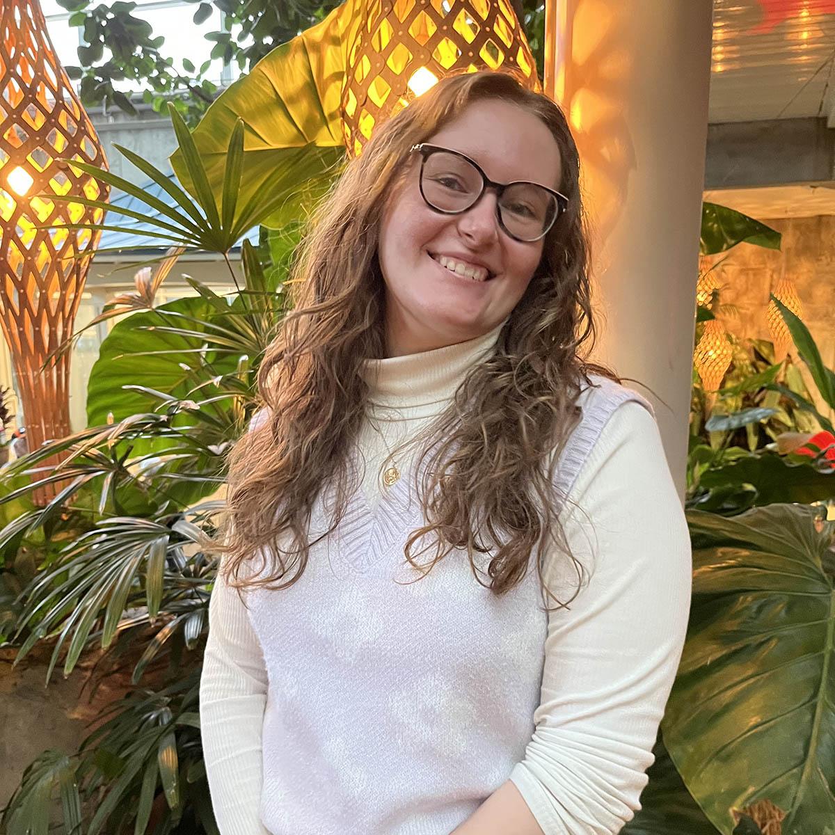 Portrait with Tara Neikirk smiling in front of large green plants